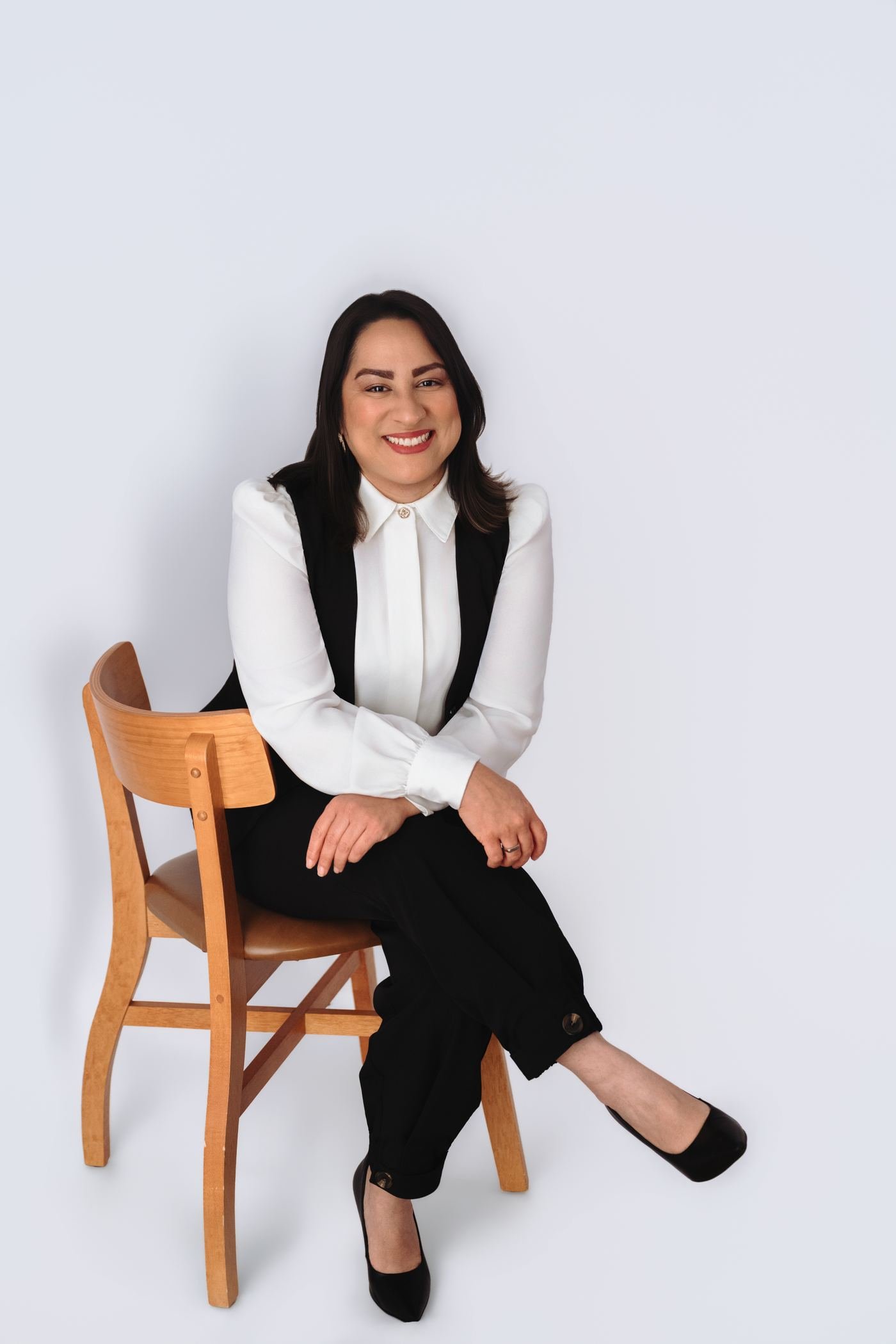 Cristina Duarte, terapeuta capilar, sorrindo sentada em uma cadeira de madeira